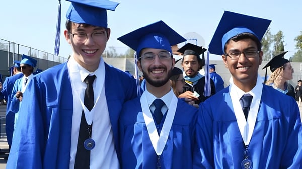 Un grupo de graduados de la A.B. Lucas Secondary School celebra al aire libre sus logros académicos en togas azules.