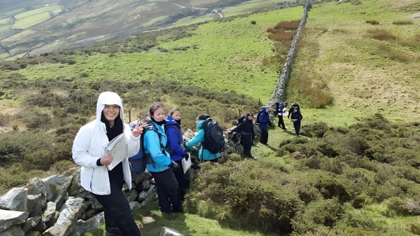 Un grupo de estudiantes del Abbey College Cambridge camina por un sendero a través de un paisaje verde con colinas y montañas al fondo.