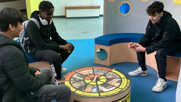 Estudiantes del Abbey College Manchester se reúnen alrededor de un gran tablero de juego redondo en el suelo para una actividad cooperativa.