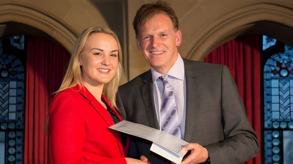 Un hombre y una mujer en ropa formal están de pie frente a coloridas ventanas de vidrio en el campus del Abbey College Manchester.