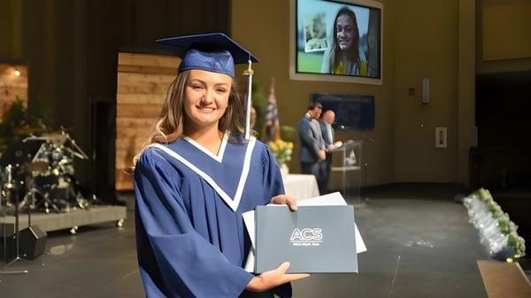 Una joven en toga de graduación sostiene su diploma en el campus de la Abbotsford Christian School.