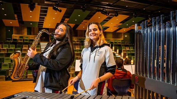 Dos personas están en un salón de música en el campus de la Aberfoyle Park High School con iluminación colorida y equipo musical de fondo.