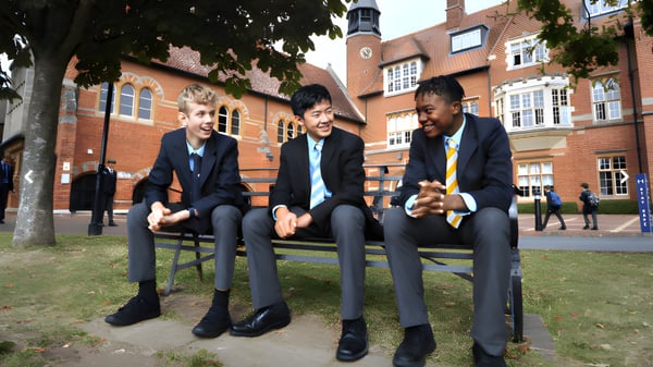 Tres estudiantes de la Abingdon School están sentados en bancos en el patio entre edificios de ladrillo.