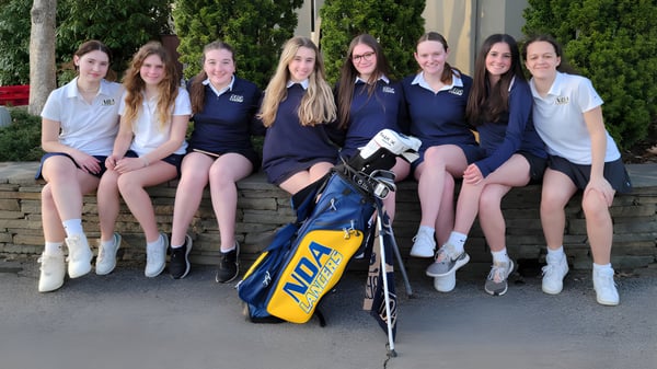 Alumnas de la Academy of Notre Dame están sentadas juntas en un muro con una bolsa de golf en primer plano.