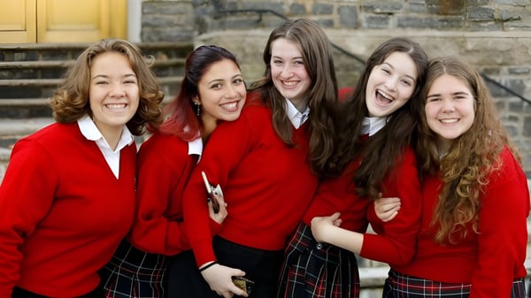 Cinco alumnas en uniformes escolares rojos posan frente a un edificio de piedra en el campus de la Academy of the New Church.