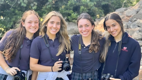 Cuatro estudiantes de la Academy of the Sacred Heart están juntas al aire libre frente a un exuberante verde.