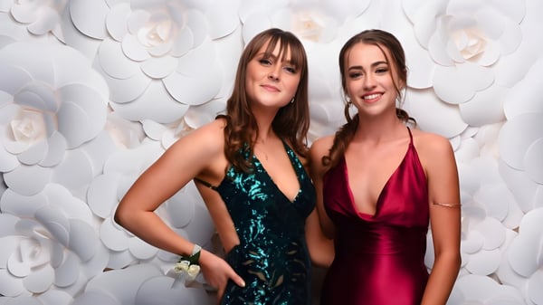 Dos estudiantes de ACG Strathallan posan en elegantes vestidos de noche frente a un fondo de grandes flores de papel blancas.