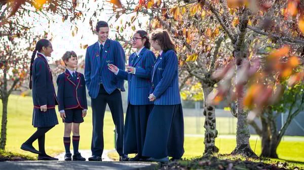 Un grupo de estudiantes en uniforme escolar está en el área exterior otoñal en el terreno de la ACG Sunderland.
