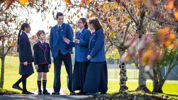 Un grupo de estudiantes en uniformes escolares está en el campus de ACG Sunderland frente a una plantación otoñal.