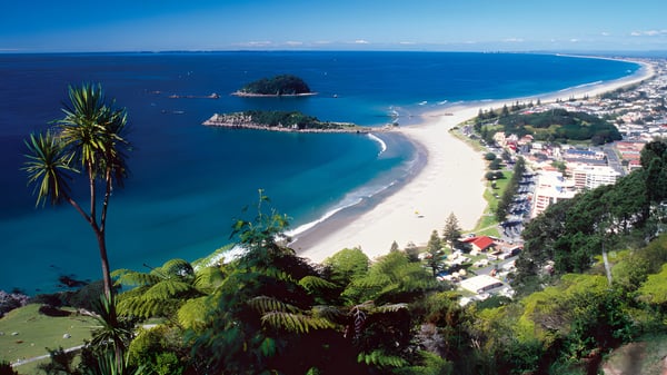 Paisaje costero con una playa en forma de media luna y vegetación tropical cerca de ACG Tauranga.