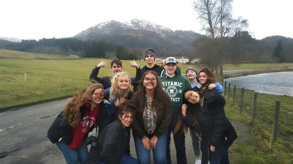 Un grupo de estudiantes de la Acton High School está junto en un área exterior pintoresca con montañas y árboles al fondo.