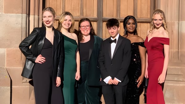 Un grupo de personas está frente a una estructura de madera en el terreno de la Adcote School.