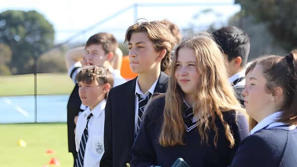 Un grupo de estudiantes de la Adelaide High School está de pie en un campo de hierba junto a los edificios escolares y árboles.