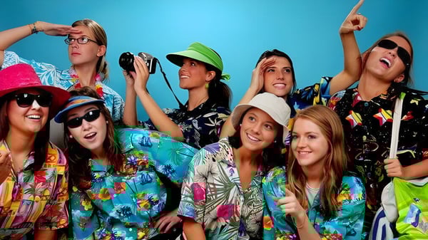 Un grupo de jóvenes mujeres posan con ropa colorida frente a un fondo azul en el campus del Aden Bowman Collegiate.