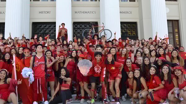 Un grupo de estudiantes de la Alameda High School en vestidos rojos posan frente a un edificio con columnas y señalizaciones.