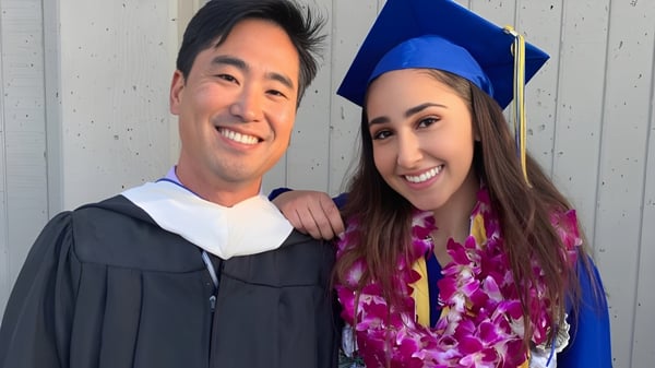Dos egresados en togas y birretes posan juntos frente a una pared de madera en el campus del Alameda Unified School District.