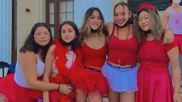 Un grupo de jóvenes mujeres con atuendos rojos posan frente a un edificio en el campus del Alameda Unified School District.