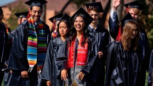 Un grupo de graduados está de pie al aire libre con vestimenta académica colorida en el campus de la Albuquerque Academy.