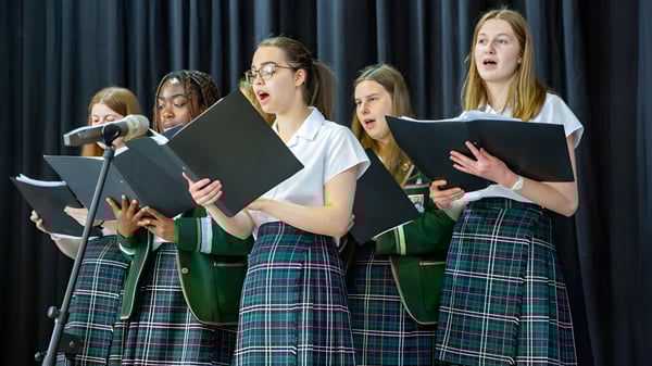 Un grupo de estudiantes de la Albyn School actúan con uniformes escolares y partituras en un escenario.