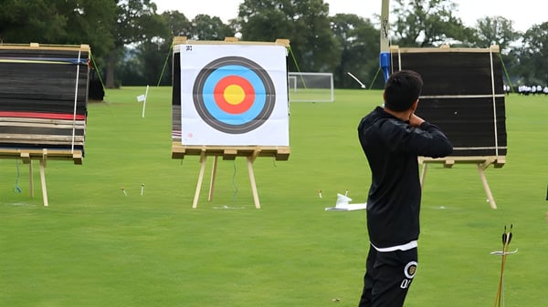 Una persona vestida de negro está frente a un objetivo de tiro con arco en un campo en el terreno de la Aldenham School.