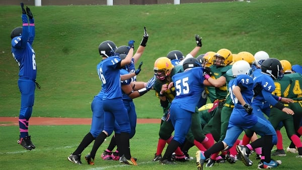 Un grupo de jugadores de fútbol americano en camisetas azules y amarillas juega en el campo de la Aldershot High School.