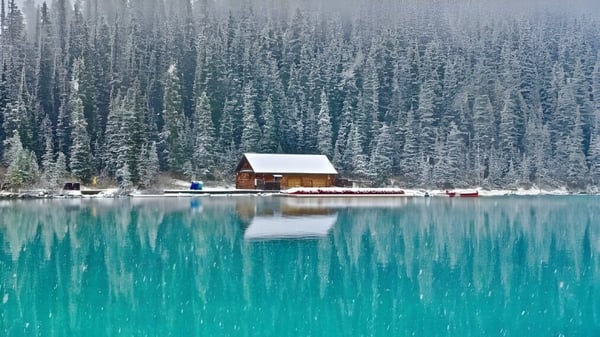Una pequeña cabaña de madera se encuentra a la orilla de un lago turquesa frente a un bosque nevado en el terreno de la Alexander Galt Regional High School.