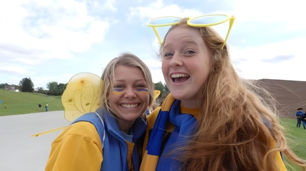Dos estudiantes de la Alexander Galt Regional High School con atuendos amarillos y azules ríen al aire libre en un espacio verde.