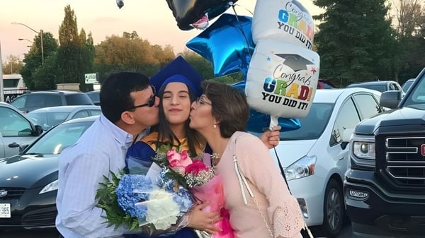 Tres personas están juntas y sonríen en el estacionamiento de la Alexander Mackenzie High School.