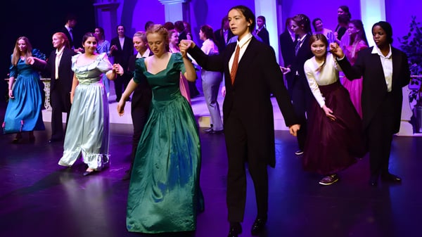 Un grupo de estudiantes elegantemente vestidos del Alexandra College en un evento festivo bajo una iluminación violeta.