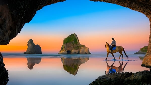 Una persona a caballo se encuentra en la playa frente a rocas durante el atardecer cerca del Alfriston College.
