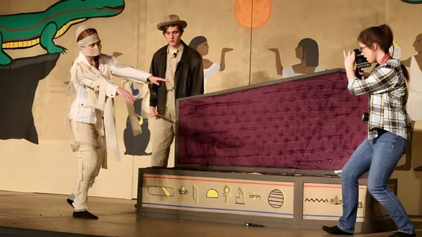 Tres personas están frente a una colorida pared de arte con un gran dinosaurio verde en el campus de la Algoma Christian High School.