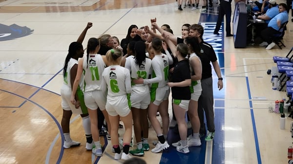 Un grupo de jugadoras de baloncesto en uniforme está en la cancha del Algonquin College con espectadores al fondo.