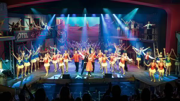 Estudiantes de la All Saints Anglican School realizan una actuación en el escenario con coloridos disfraces y una iluminación dinámica.