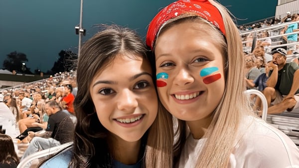 Dos estudiantes de la Alma High School posan en el estadio lleno con numerosos espectadores al fondo.