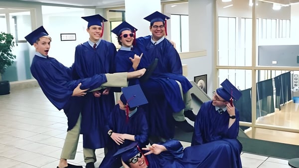 Un grupo de graduados de la American Heritage Academy está en el pasillo con togas y birretes azules después de la ceremonia de graduación.