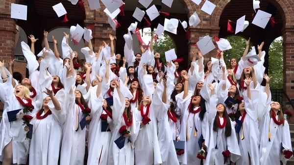 Un grupo de estudiantes en túnicas blancas sostiene banderas rojas y blancas en el terreno de Annie Wright Schools.