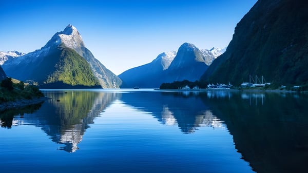 Montañas con picos nevados se reflejan en un lago tranquilo cerca del Aorere College.