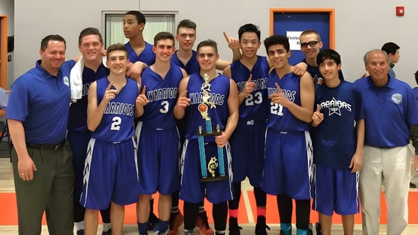 Un grupo de estudiantes de baloncesto de la Apple Valley Christian School en camisetas azules posan en un gimnasio.