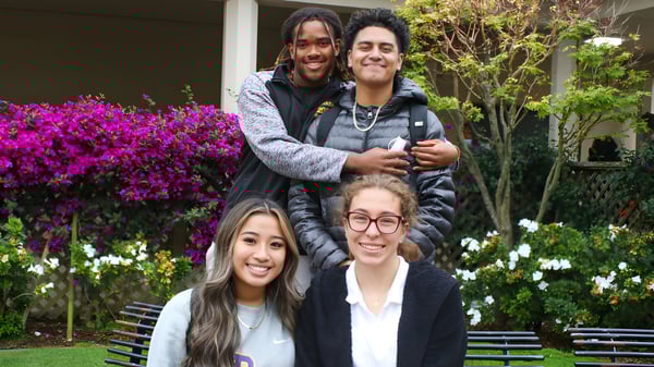 Un grupo de cuatro estudiantes posan juntos en un jardín con flores de colores en el terreno de la Archbishop Riordan High School.