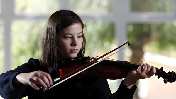 Una alumna de la Archbishop's School toca la violín concentrada frente a un fondo natural desenfocado.