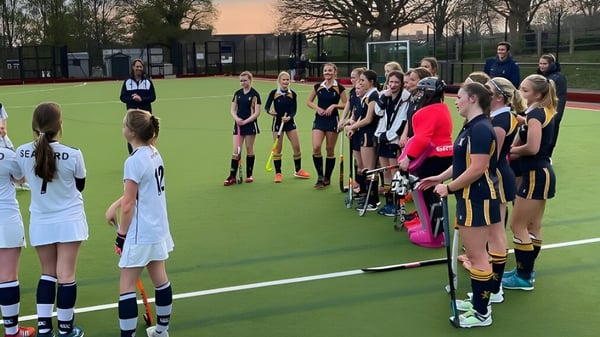 Un grupo de jóvenes deportistas está en el campo de deportes del Ardingly College con árboles y edificios al fondo.