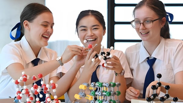 Tres alumnas de la Ardscoil Mhuire examinan riendo coloridos modelos de moléculas en un laboratorio.