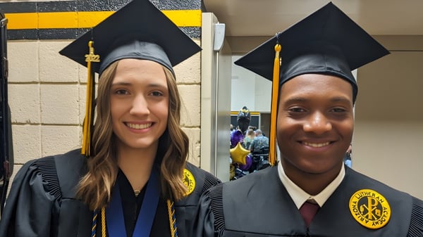 Dos graduados en togas y birretes posan en el campus de la Arizona Lutheran Academy para una foto.