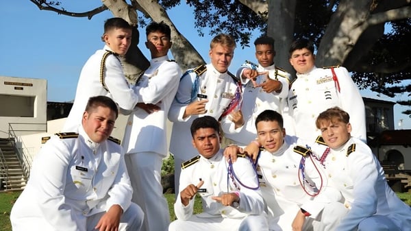 Un grupo de estudiantes de la Army and Navy Academy posan al aire libre frente a árboles y un edificio.