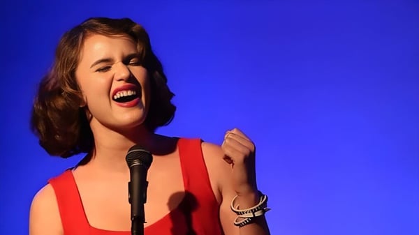 Una estudiante de la Arroyo Pacific Academy canta apasionadamente en un micrófono frente a un fondo azul.