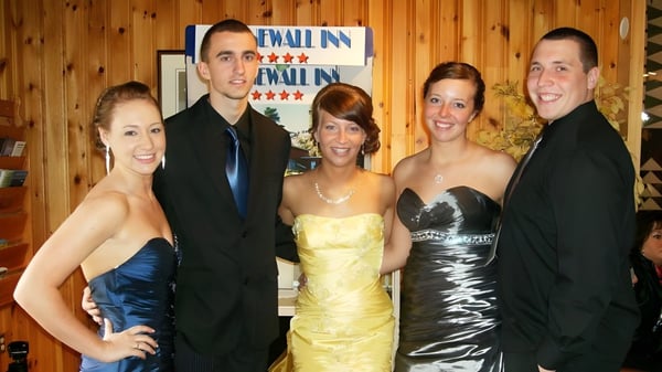 Un grupo de cinco personas posan frente a la pared de madera con el letrero de Wall Inn en el terreno de la Ascension Collegiate.