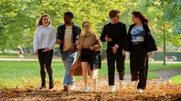 Un grupo de alumnas y alumnos del Ashbourne College pasea juntos por un camino rodeado de naturaleza verde.
