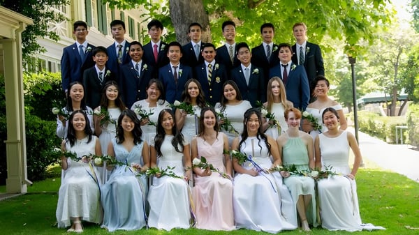 Un grupo de estudiantes del Ashbury College está vestido formalmente en un área exterior verde con árboles de fondo.