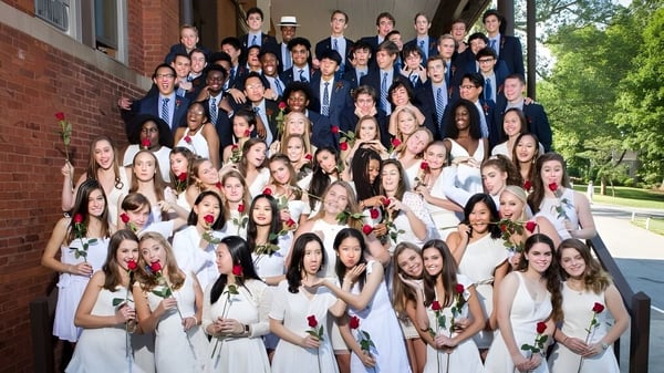 Un grupo de estudiantes vestidos formalmente se reúne frente al edificio de ladrillo de la Asheville School.