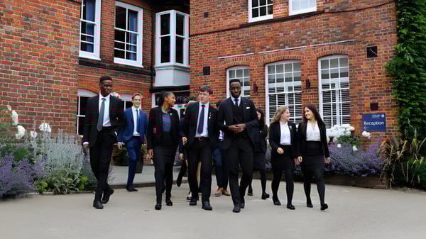 Un grupo de personas camina juntas frente a un edificio de ladrillo en el campus de la Ashford School.